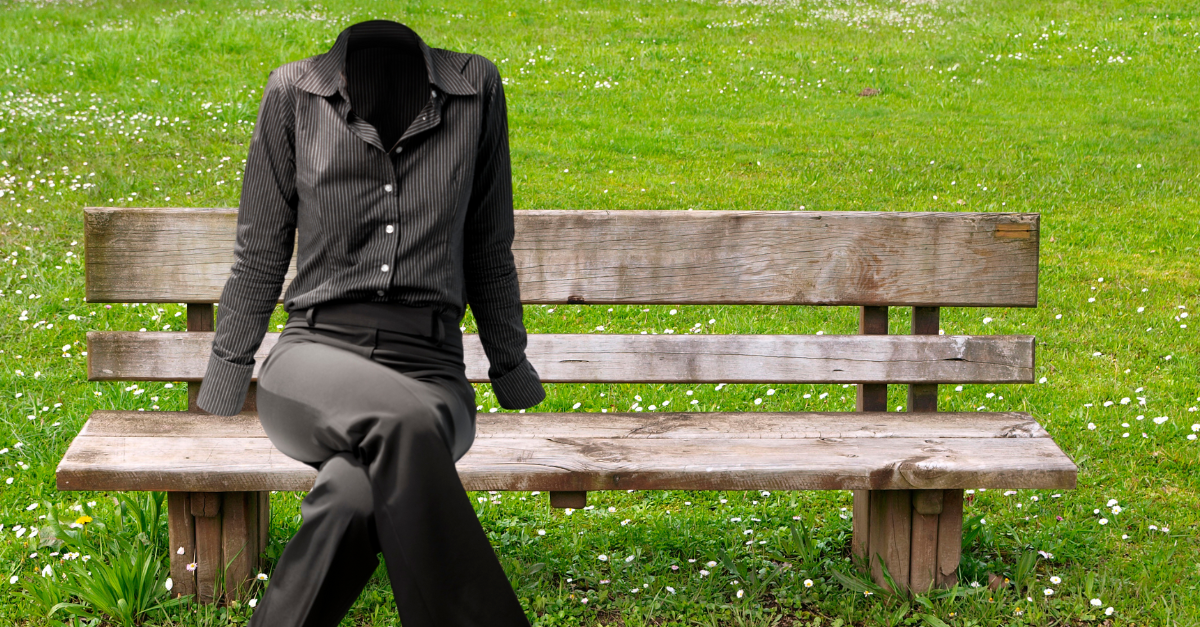 A woman in a black pants suit sits on a park bench on green grass. Her head and hands are invisble.